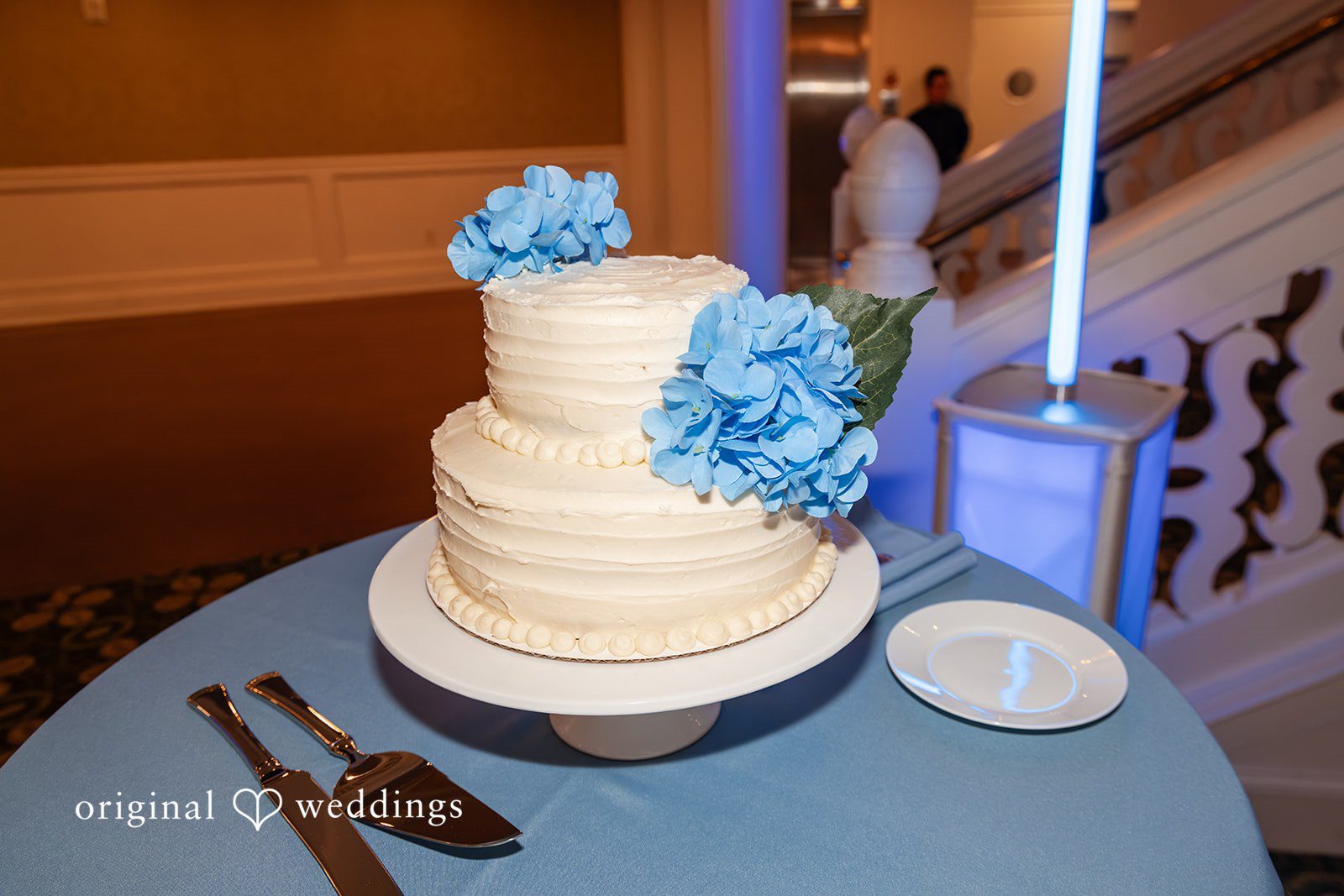 Mark + Caroline A three-tiered white wedding cake decorated with blue flowers.