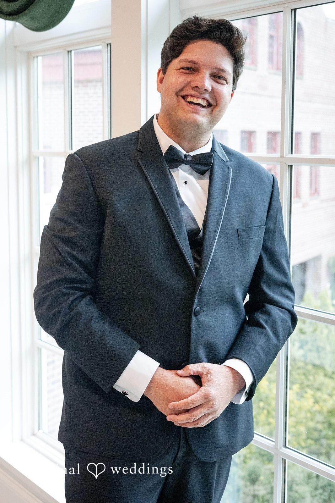 Mark + Caroline A portrait of a groom smiling in a dark suit and bow tie.