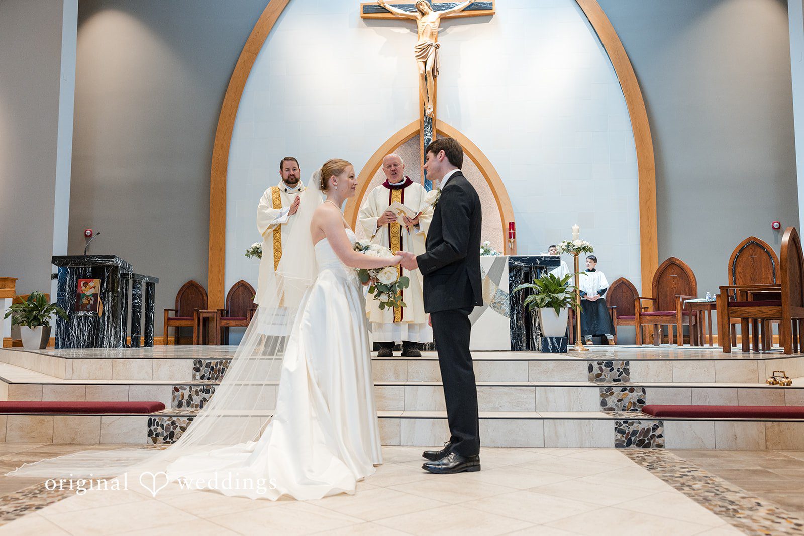 Cora + Michael Romantic couple holding hands while looking at each other before priest at the Emerald Event Center