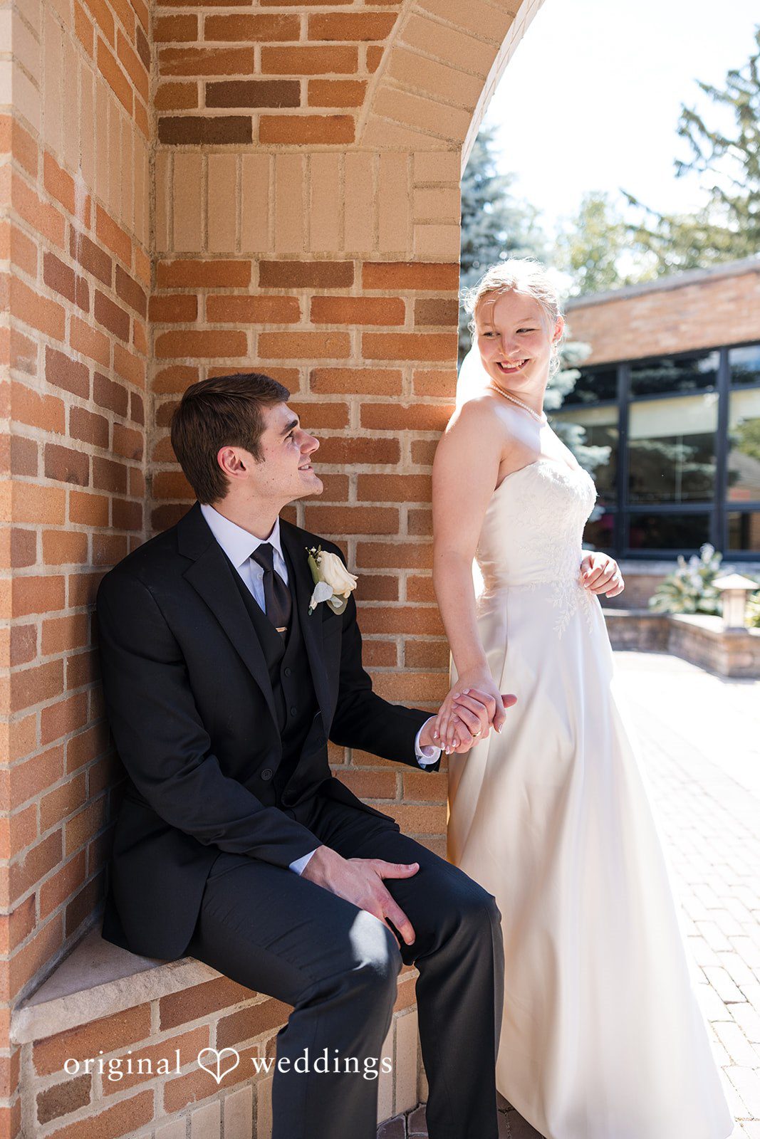 Cora + Michael Elegant groom sitting and bride standing portrait while smiling at the Emerald Event Center