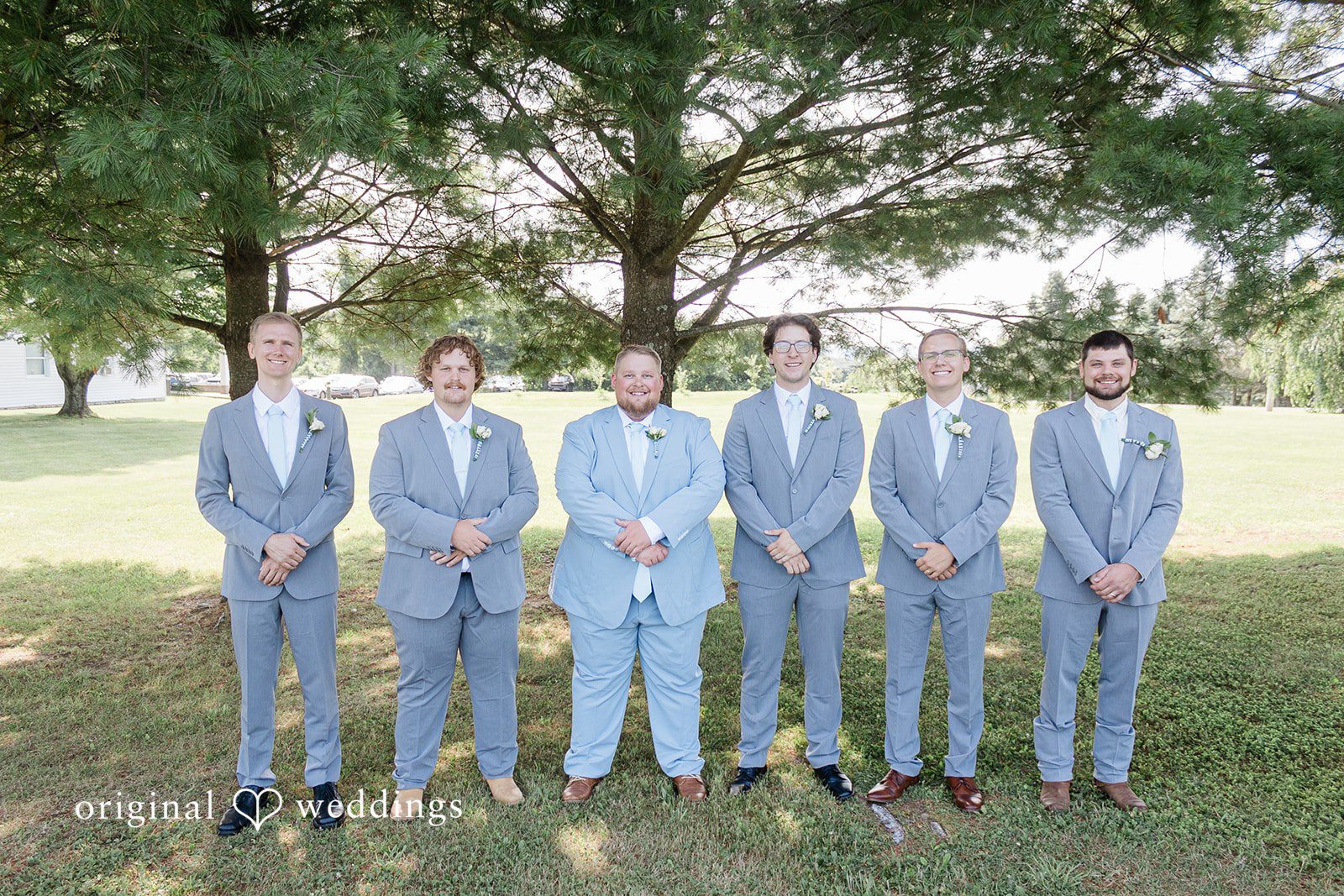 Michaela + Jake Five groomsmen in light blue suits stand side-by-side in a grassy area.