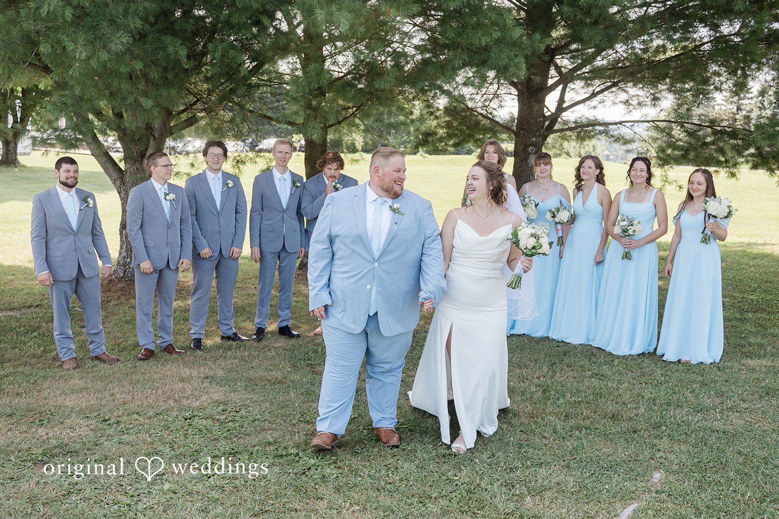 Michaela + Jake A full wedding party poses together in a field under a shady tree.