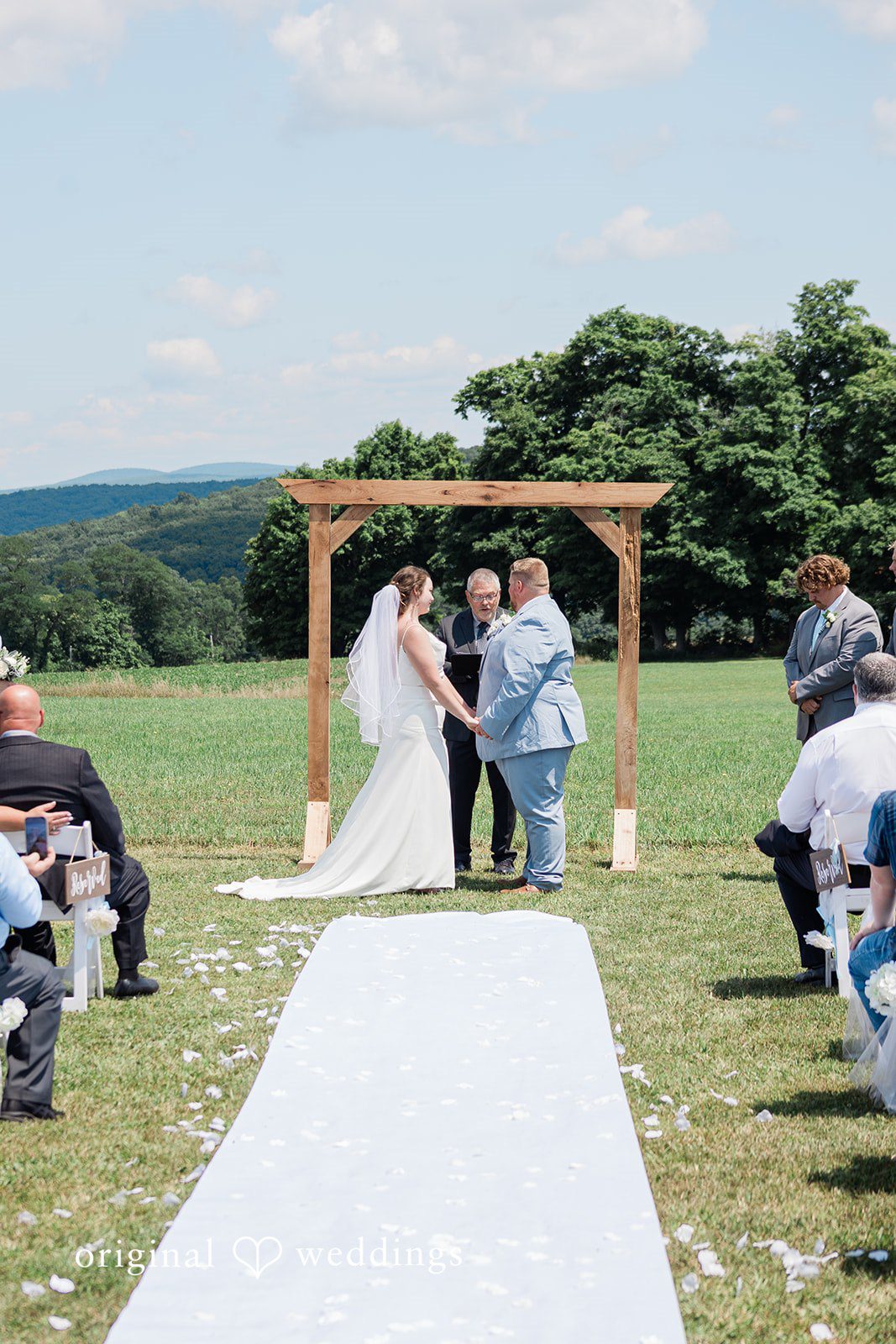 Michaela + Jake A wide view of a wedding ceremony with guests seated in a field.