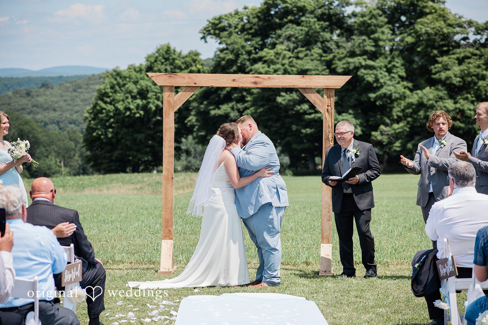 Michaela + Jake A bride and groom stand together and kissing each other under a wooden arch during their vows.