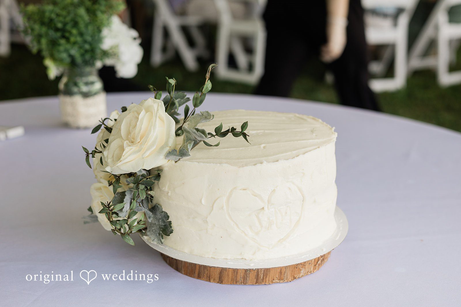 Michaela + Jake A rustic single-tier white wedding cake sits on a wooden slice stand.