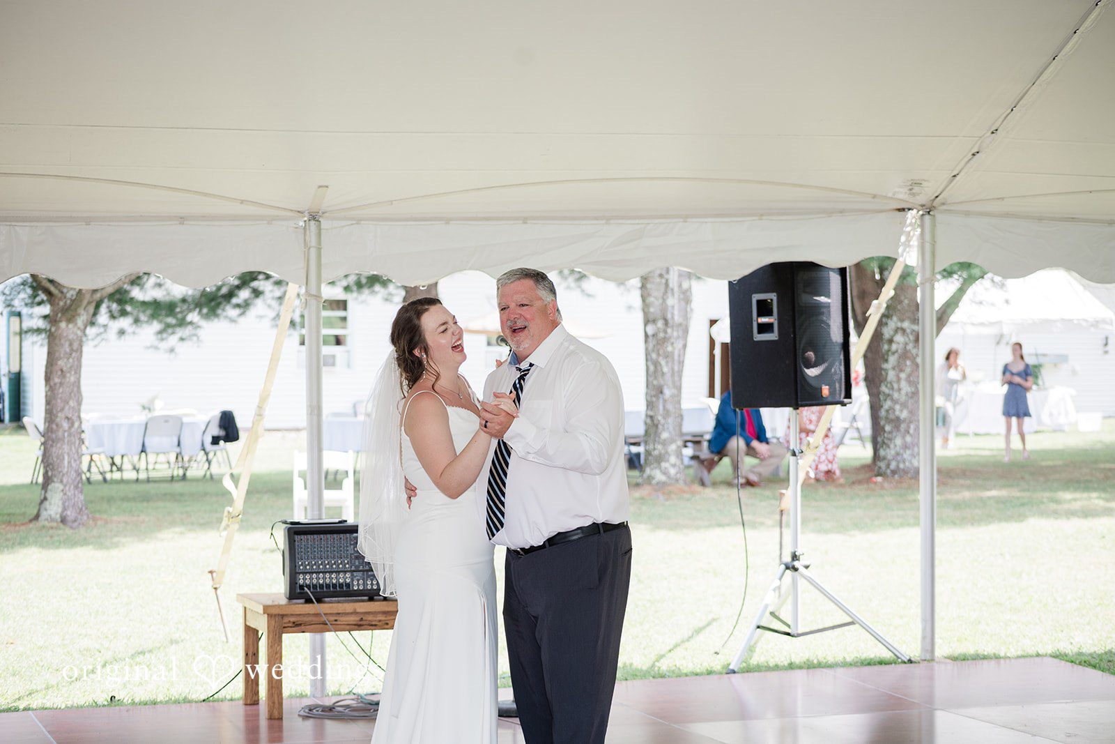 Michaela + Jake A bride and a man in a white shirt laugh joyfully while dancing under a white reception tent.