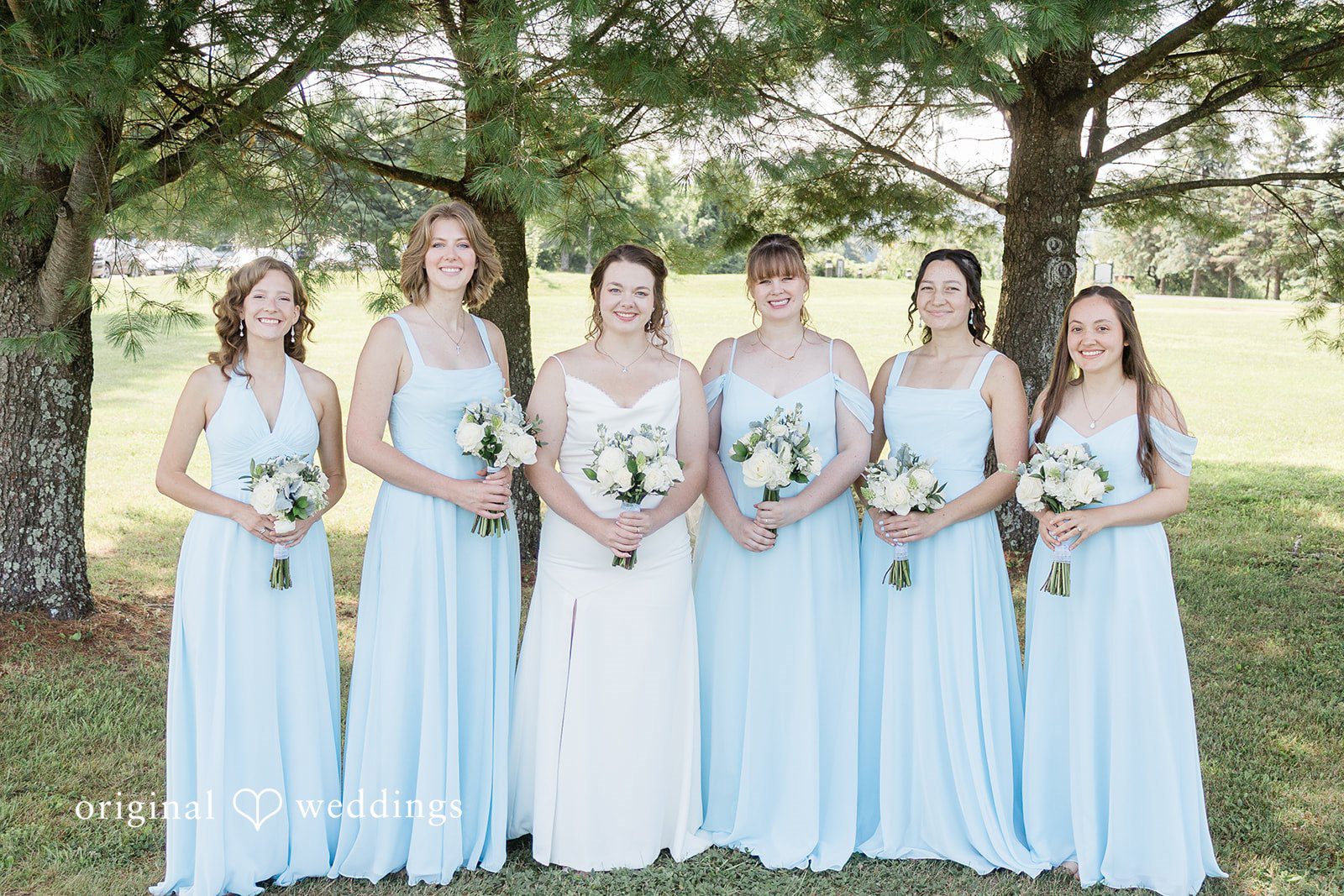 Michaela + Jake Bride and bridesmaids dressed in light blue gowns stand side-by-side in a line.