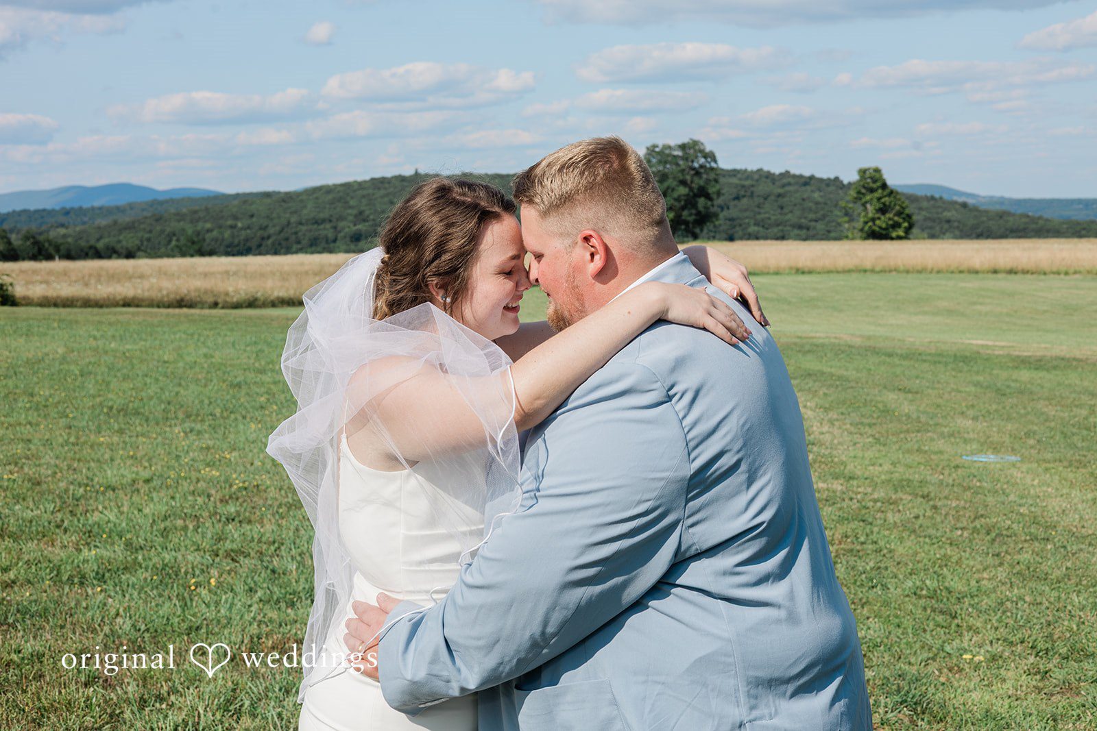 Michaela + Jake A groom embraces his bride in a field while she smiles happily.