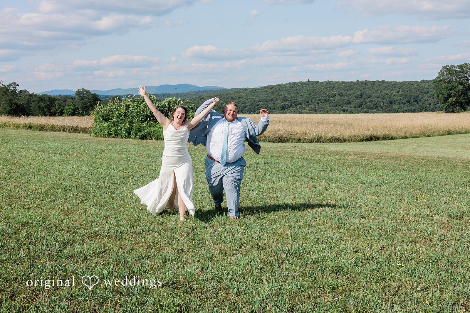 Michaela + Jake A bride and groom joyfully cheer with their arms raised in a field.
