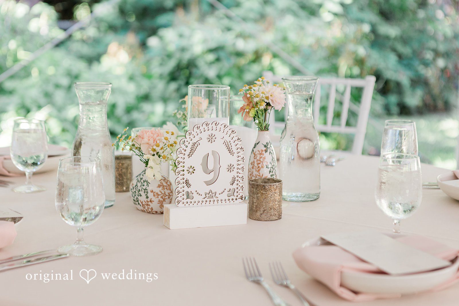 Table setting decorated with tall glassware, candles, and light linens.