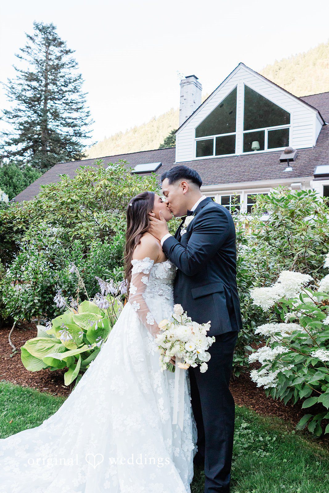 Groom kissing the bride near garden bushes.