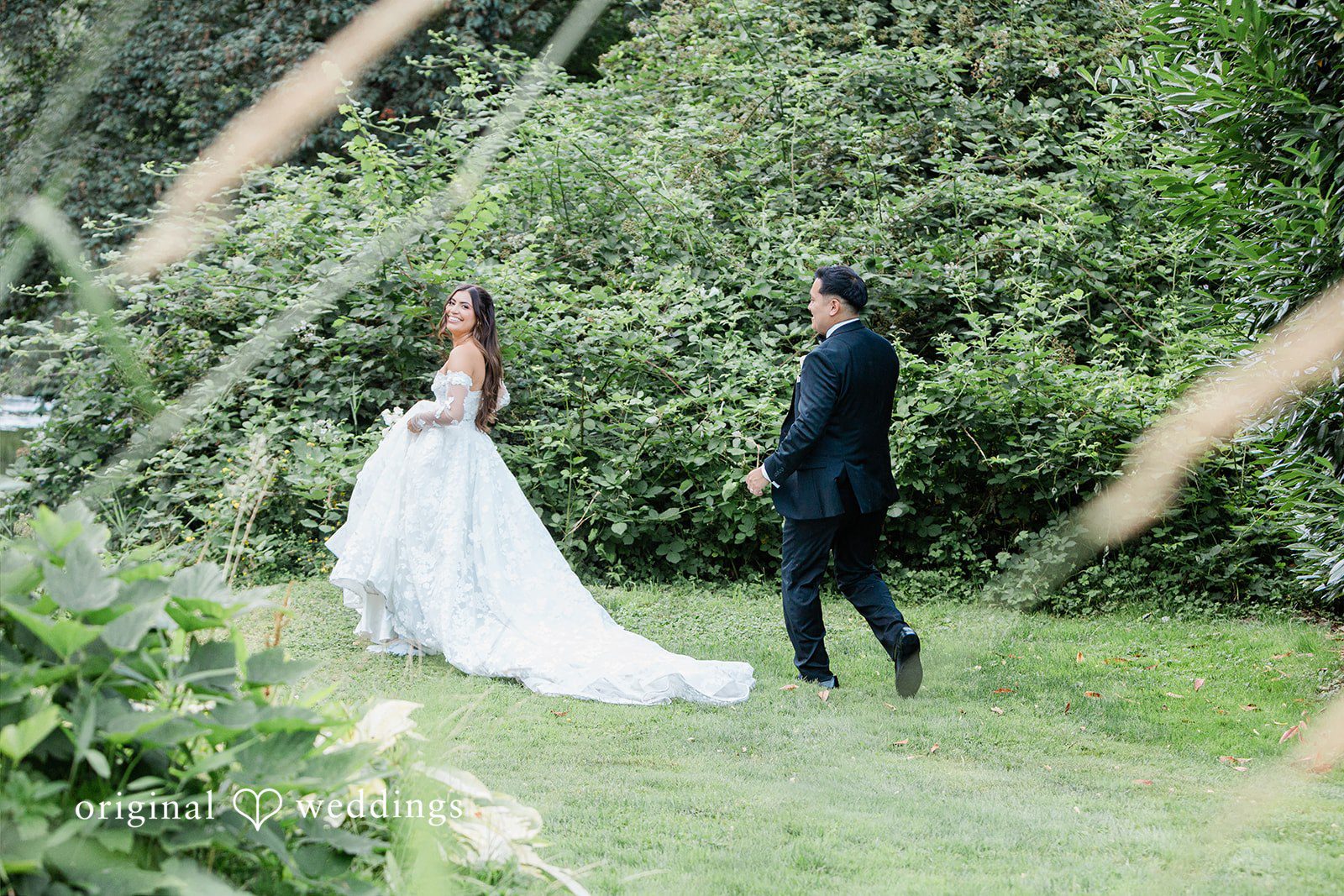 Bride walking along a path while the groom looks on.