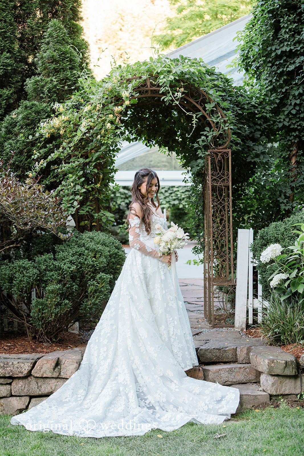 Bride in a flowing wedding dress walking through a garden archway.
