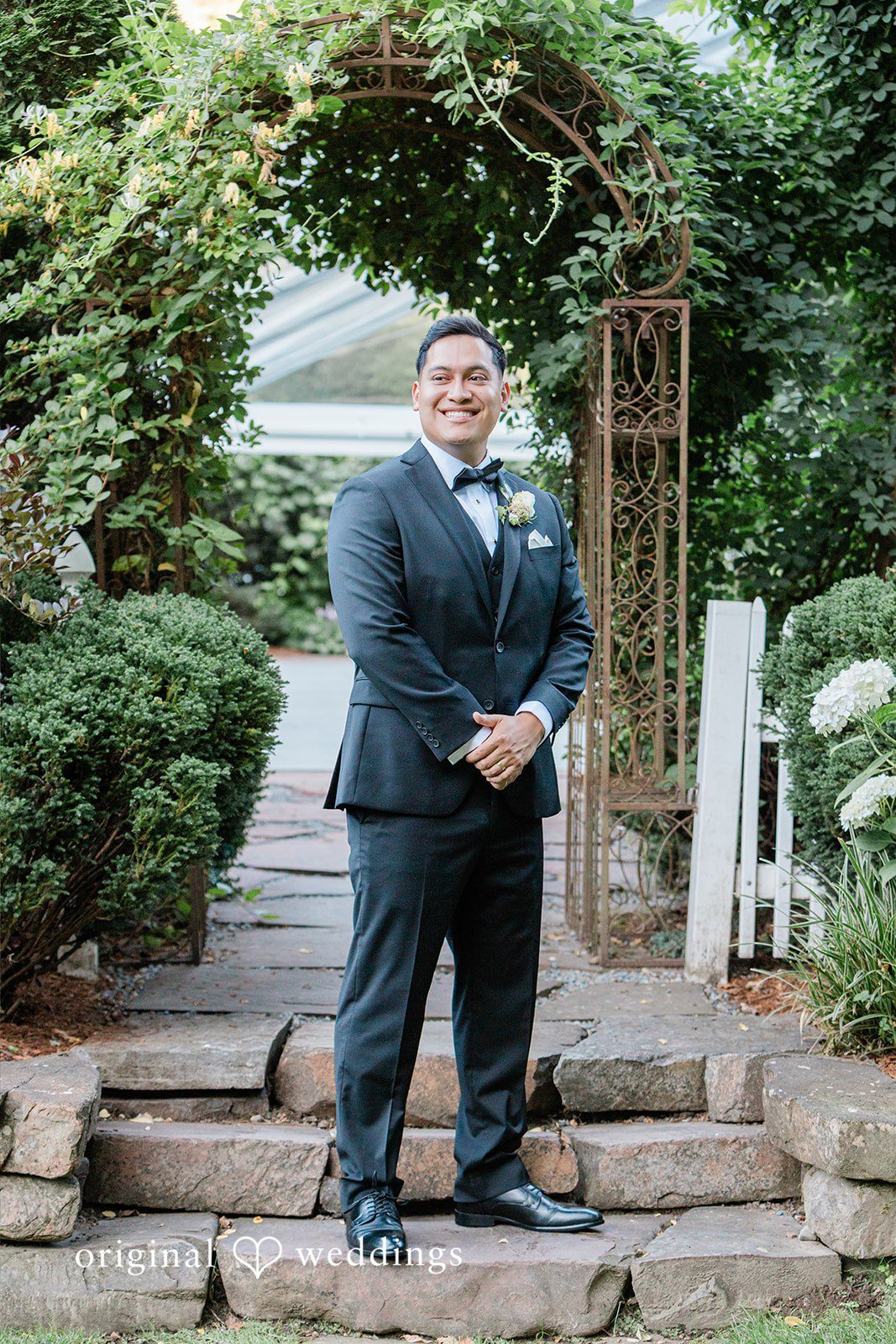 Groom wearing a dark suit standing on a stone path.