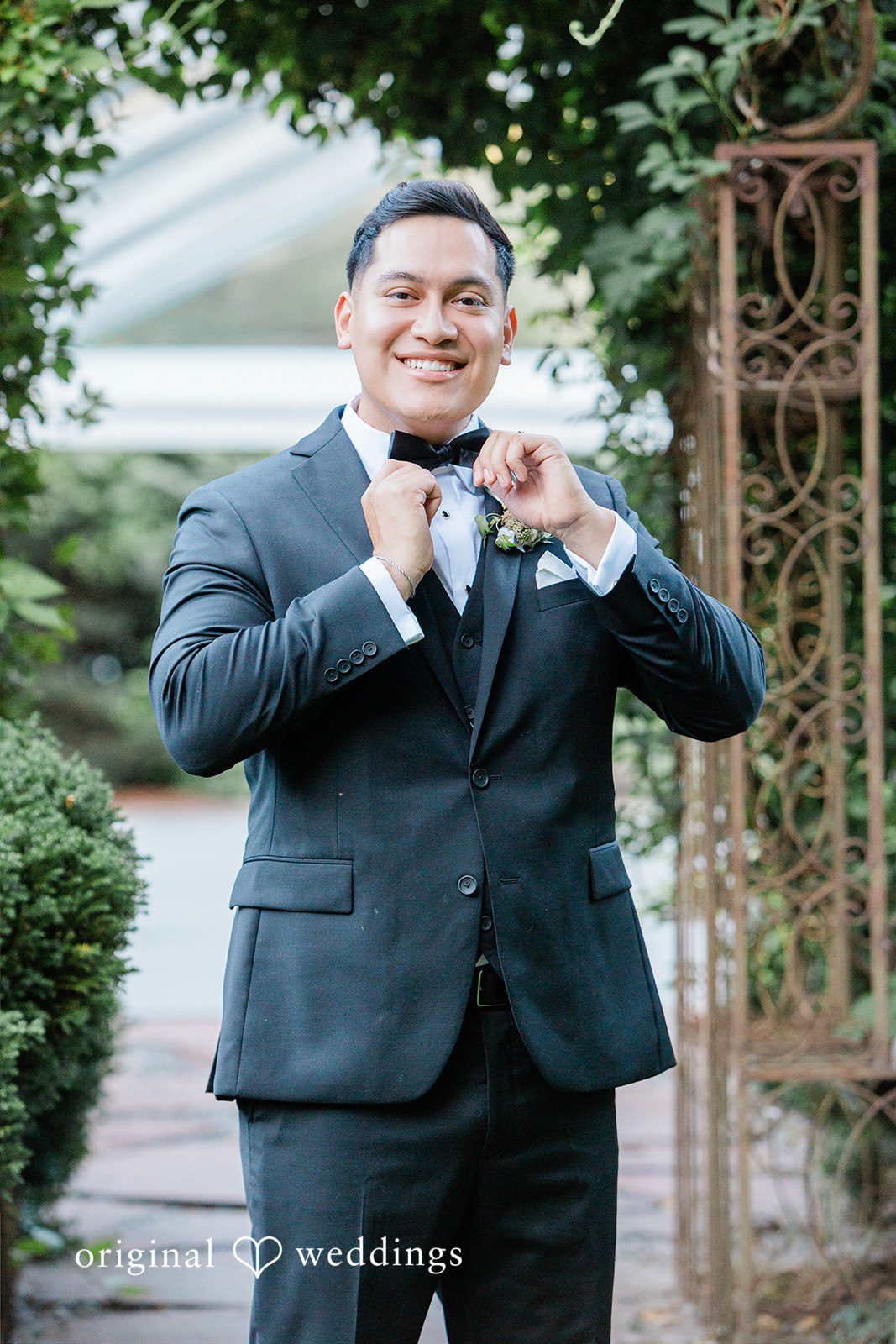 Groom smiling while adjusting his bowtie.