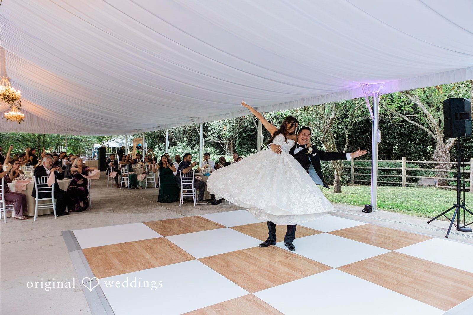 Bride spinning on a checkered dance floor under a reception tent.