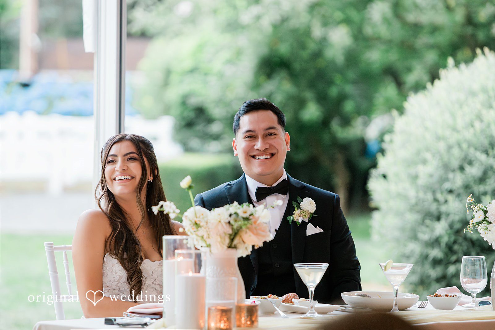 Bride and groom smiling while seated together at their reception table.