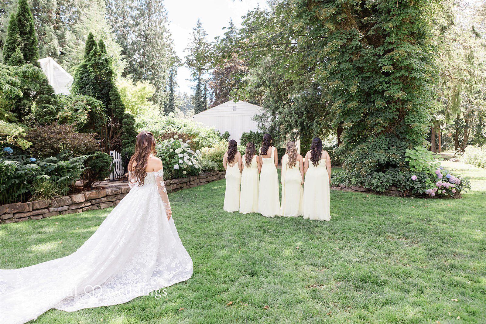 Bride posing on a lawn with bridesmaids lined up behind her.