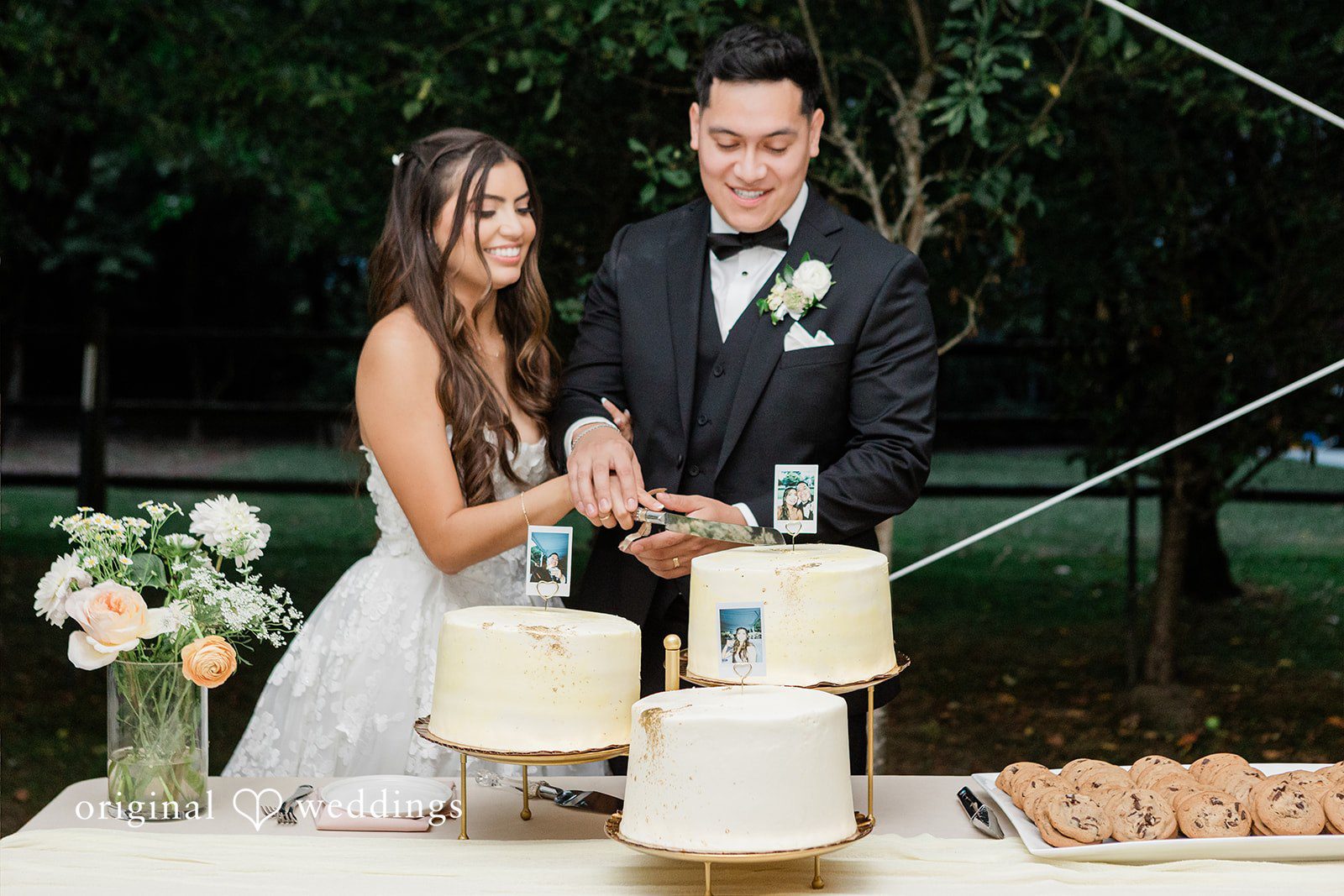 Bride and groom standing together behind a multi-tiered wedding cake.