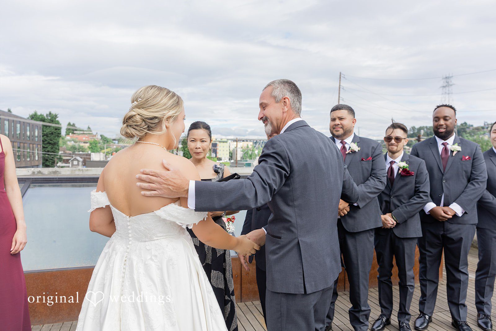 Michelle + Eric A man in a dark suit places a hand on a bride's shoulder during a rooftop wedding ceremony.