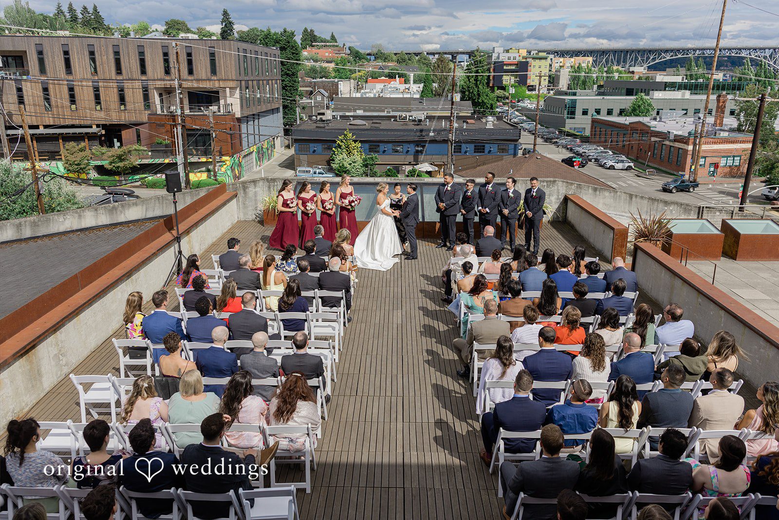 Michelle + Eric An overhead wide shot of a rooftop wedding ceremony filled with seated guests.
