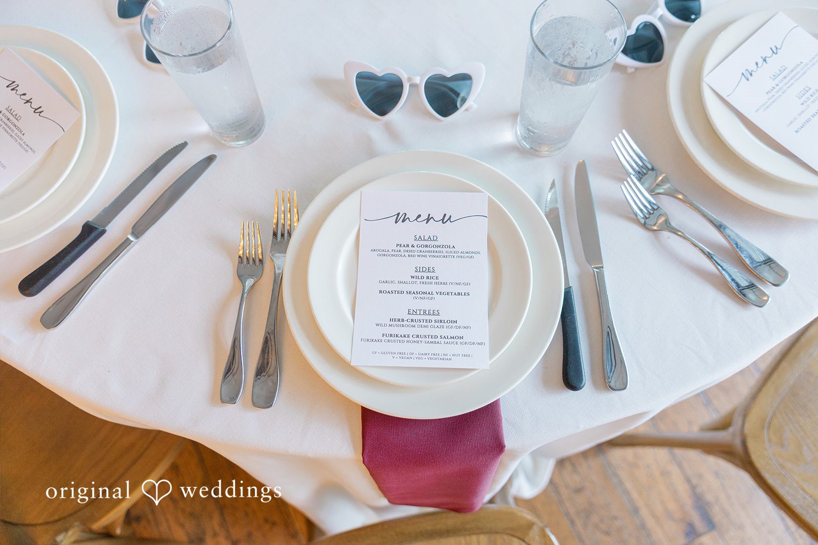 Michelle + Eric A top-down view of a wedding table setting with a white plate, menu card, and silverware.