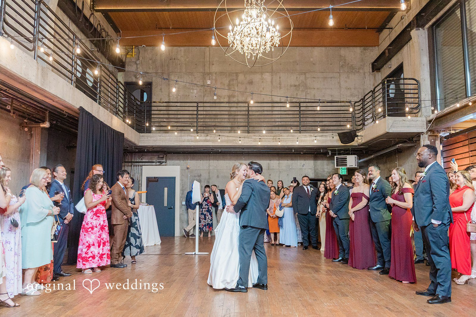 Michelle + Eric A wide shot of a bride and groom dancing in the center of a spacious rustic reception hall.