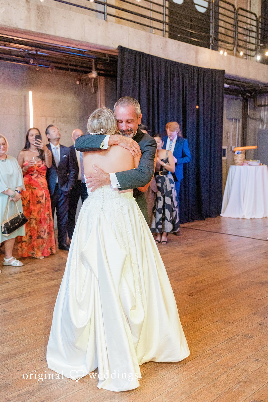 Michelle + Eric A bride and a man in a dark suit share an emotional embrace on a wooden dance floor during a wedding reception.