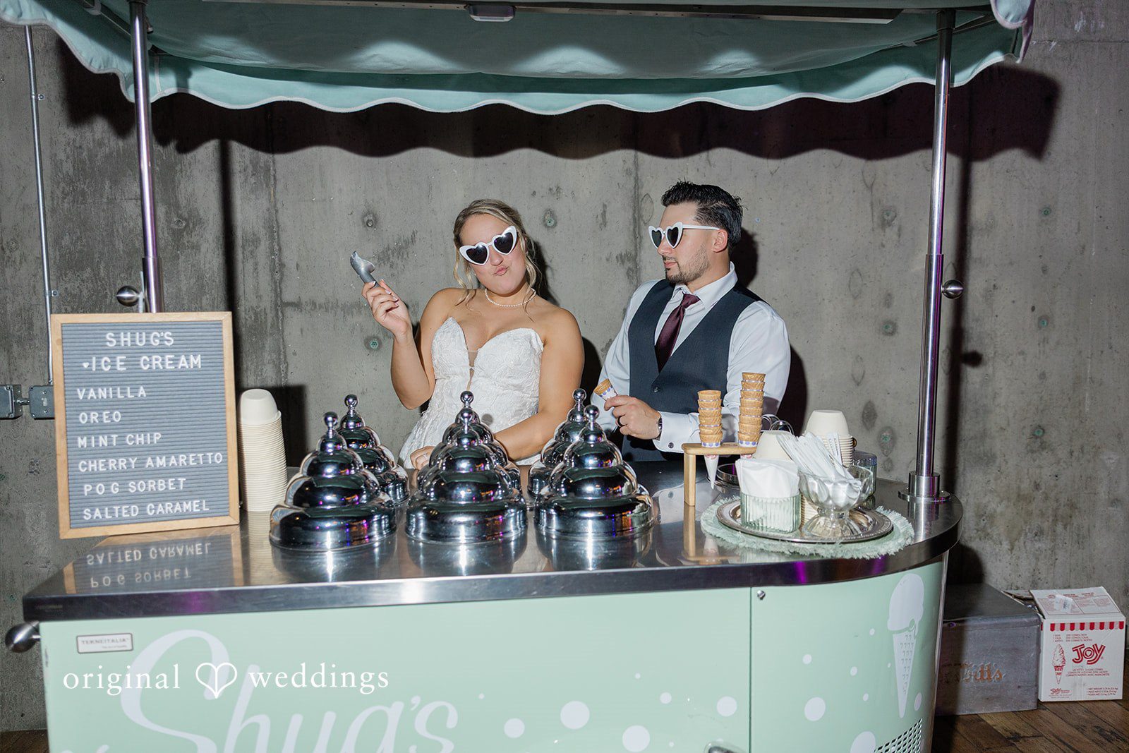 Michelle + Eric A bride and groom wearing sunglasses and posing behind a vintage mobile food or drink cart.