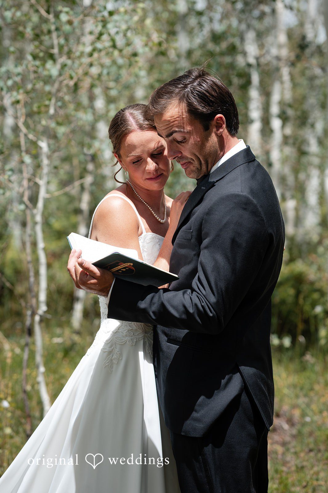 Emilia + Charlie A bride and groom reading vows to each other in a wooded area.