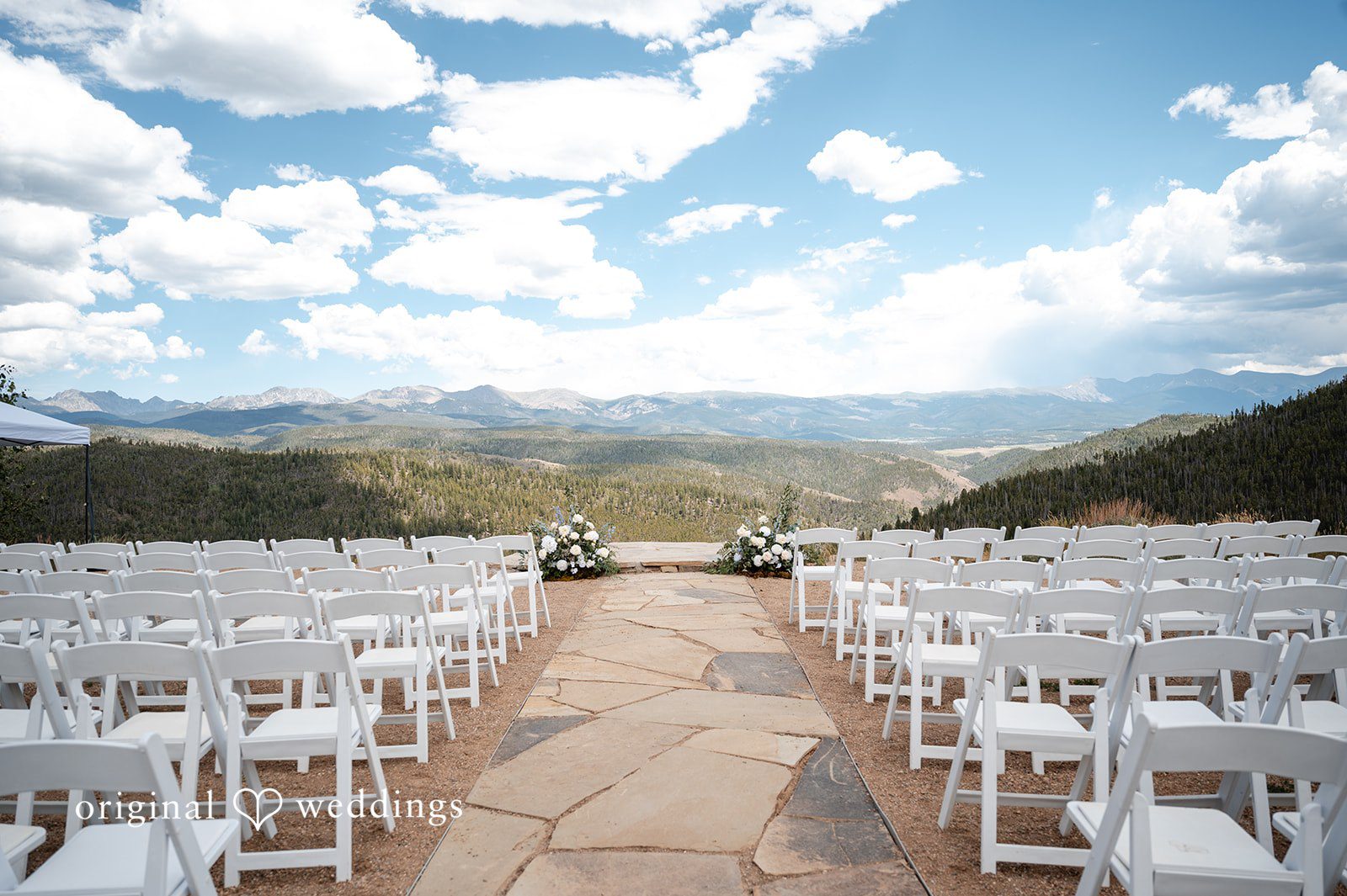 Emilia + Charlie Rows of white chairs set up for a wedding ceremony with mountains in the background.