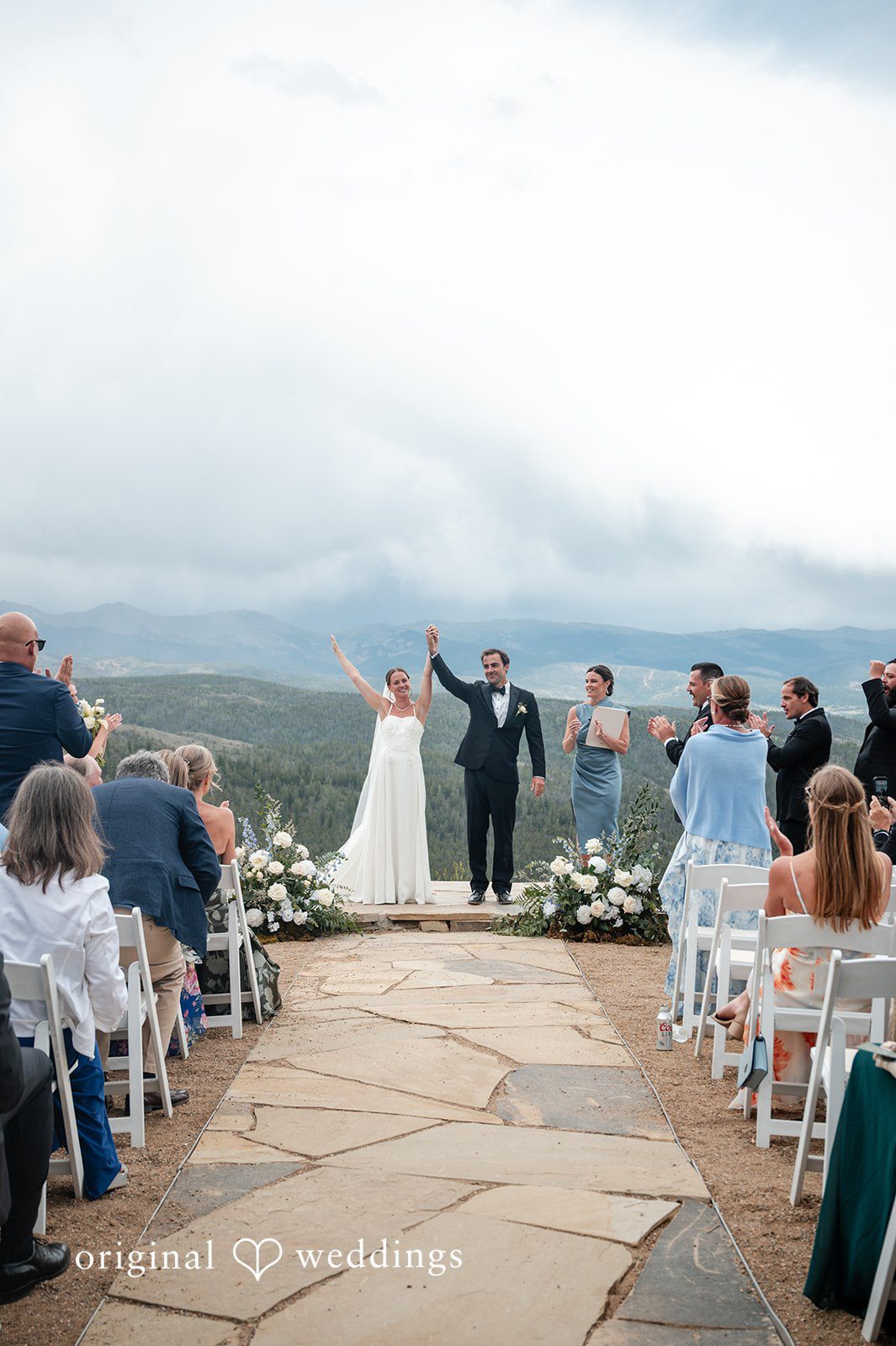 Emilia + Charlie A bride and groom raising their hands in celebration in front of seated guests.