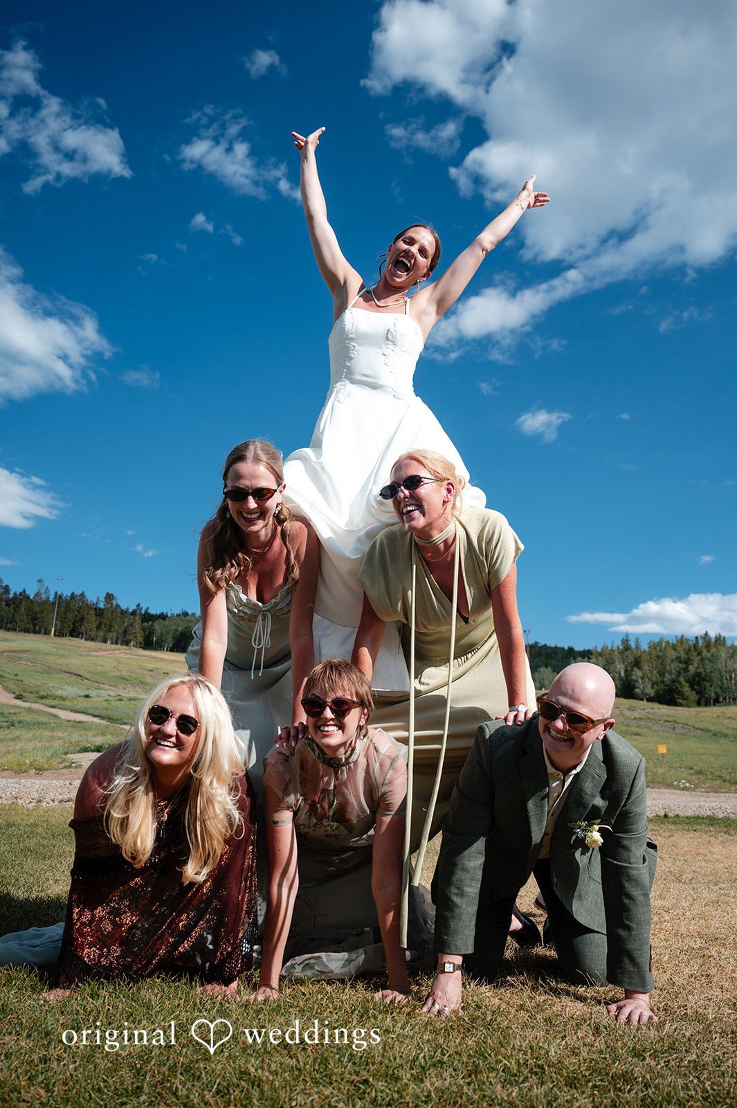 Emilia + Charlie A group of wedding guests dynamically posing together on a grassy hill.