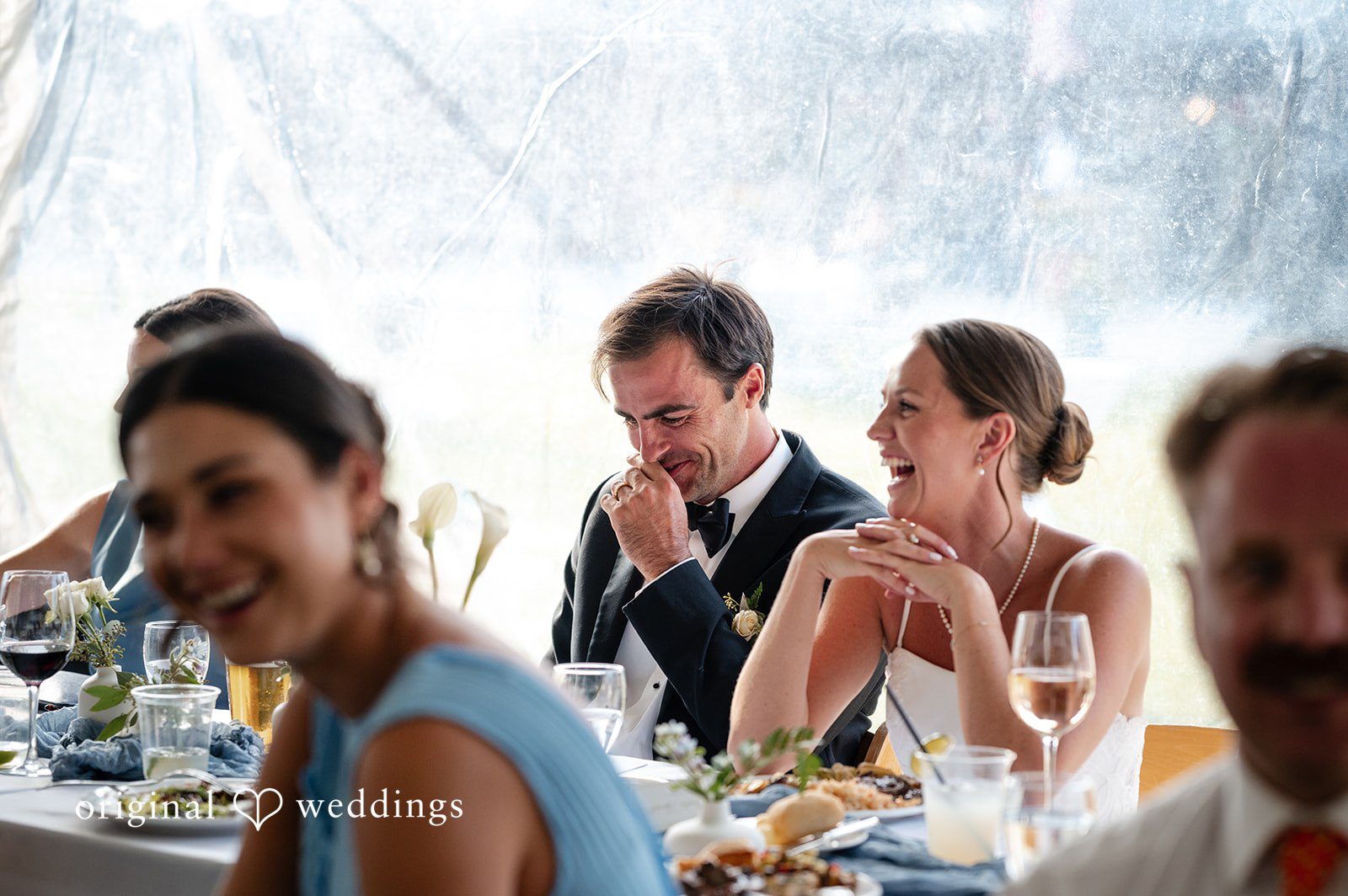 Emilia + Charlie Wedding guests smiling and chatting while seated at a reception dinner table.