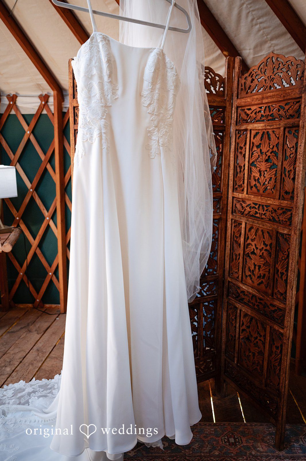 Emilia + Charlie A white wedding dress hanging up inside a rustic venue.