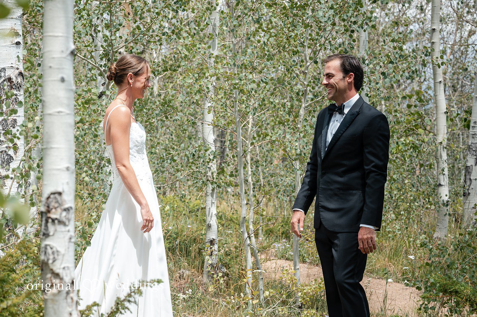 Emilia + Charlie A bride and groom facing each other in a forest of birch trees.
