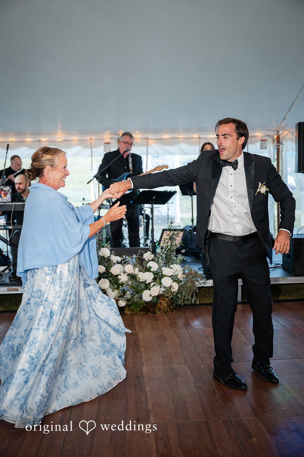 Emilia + Charlie A woman in a blue patterned dress dancing with a man in a tuxedo.