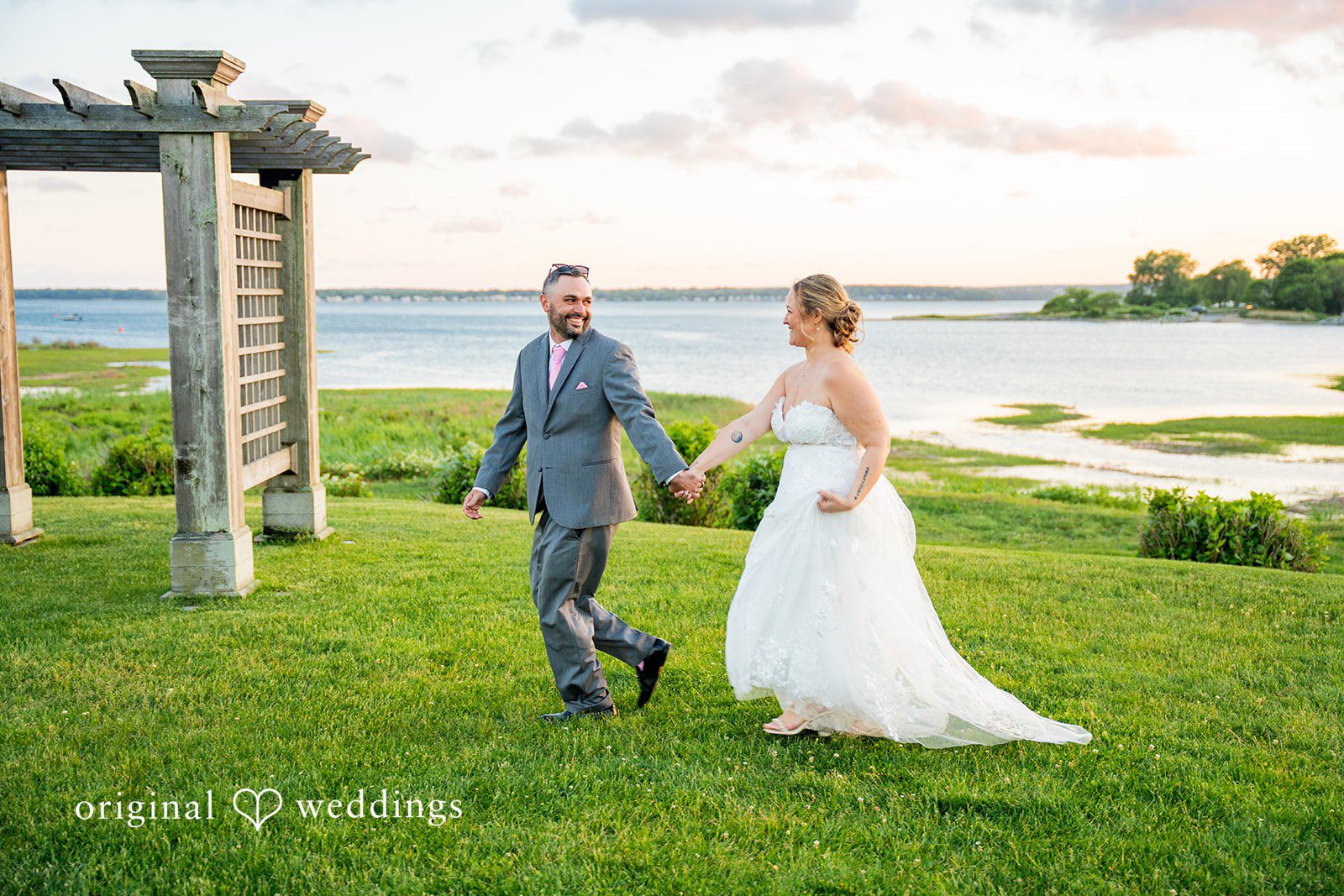 Alex + Courtney A bride and groom holding hands while walking through a grassy field.