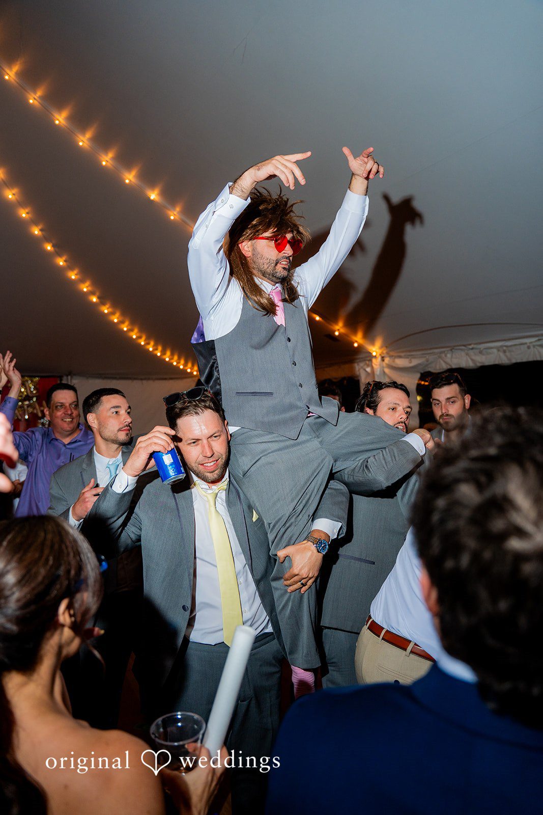 Alex + Courtney A man in a vest jumping high while dancing at a reception.