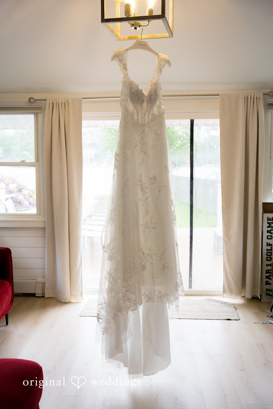 Alex + Courtney A white wedding gown hanging in front of a bright window.