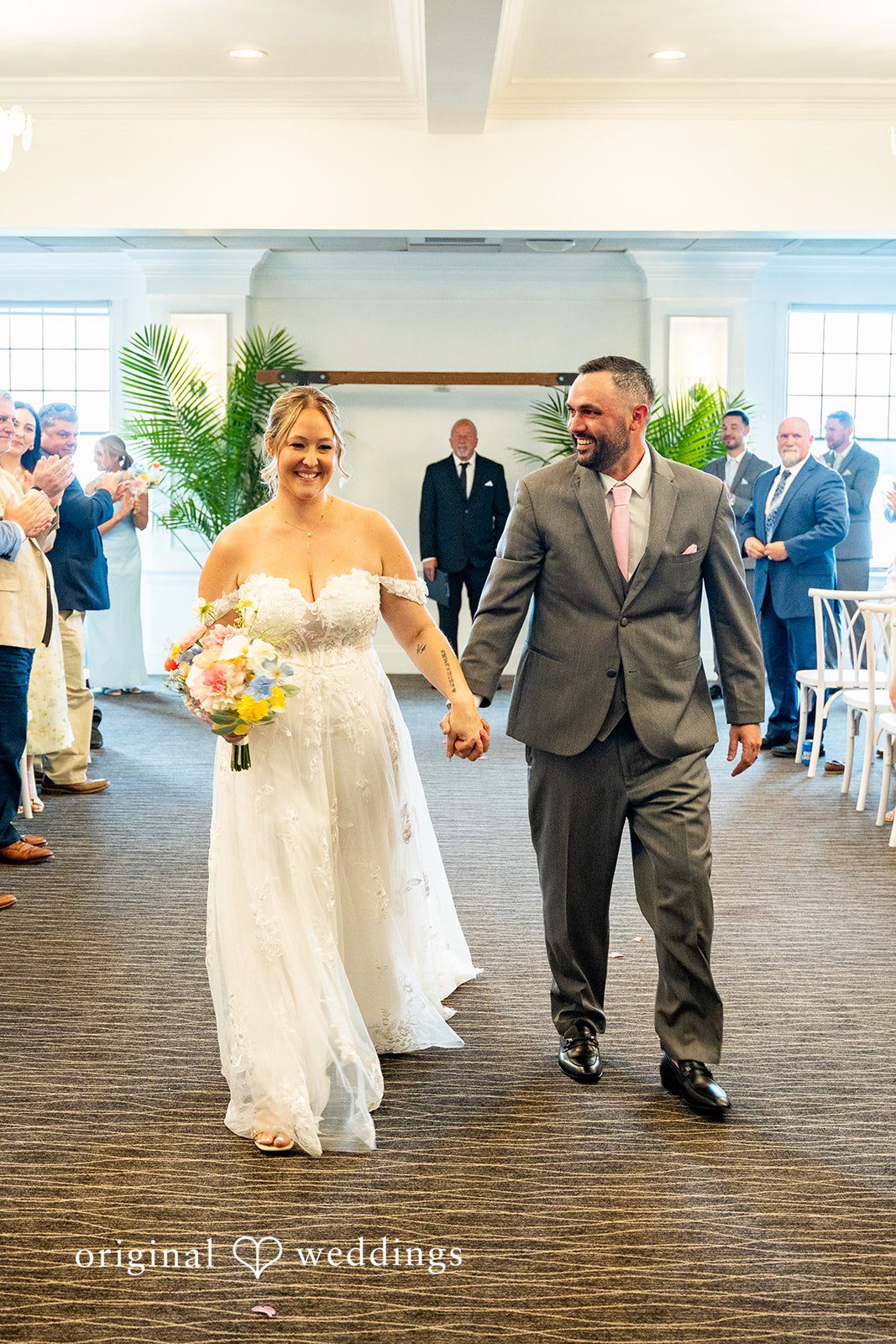 Alex + Courtney A bride and groom smiling and walking hand-in-hand together.