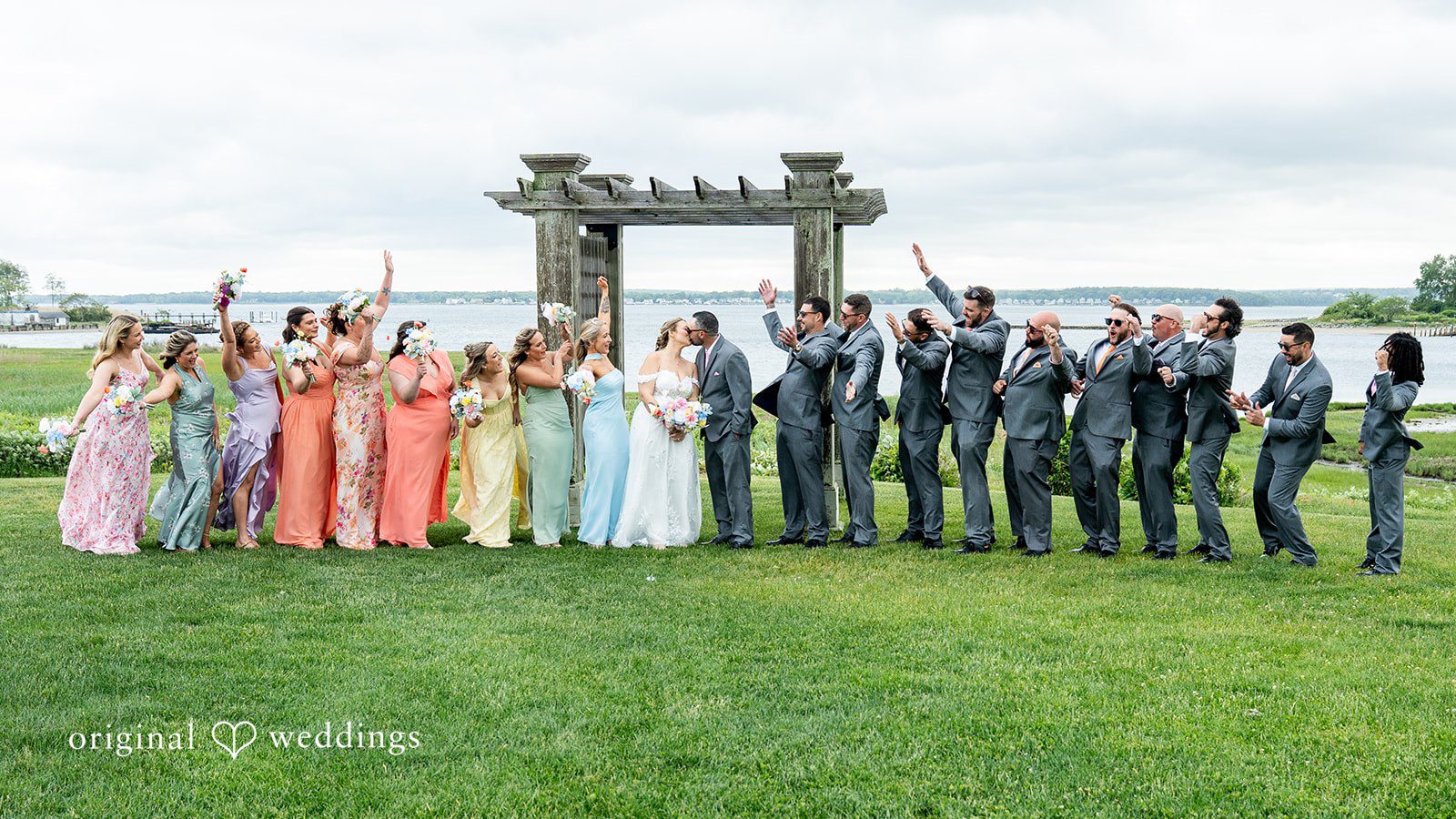 Alex + Courtney A large wedding party standing in a line on a grassy field.