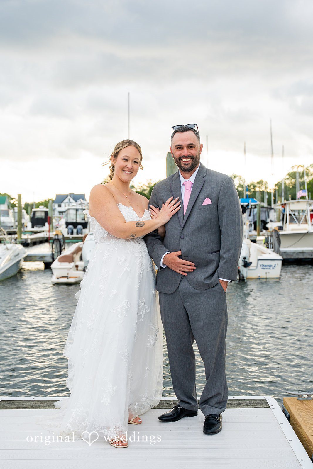 Alex + Courtney A bride and groom posing together on a white dock by boats.