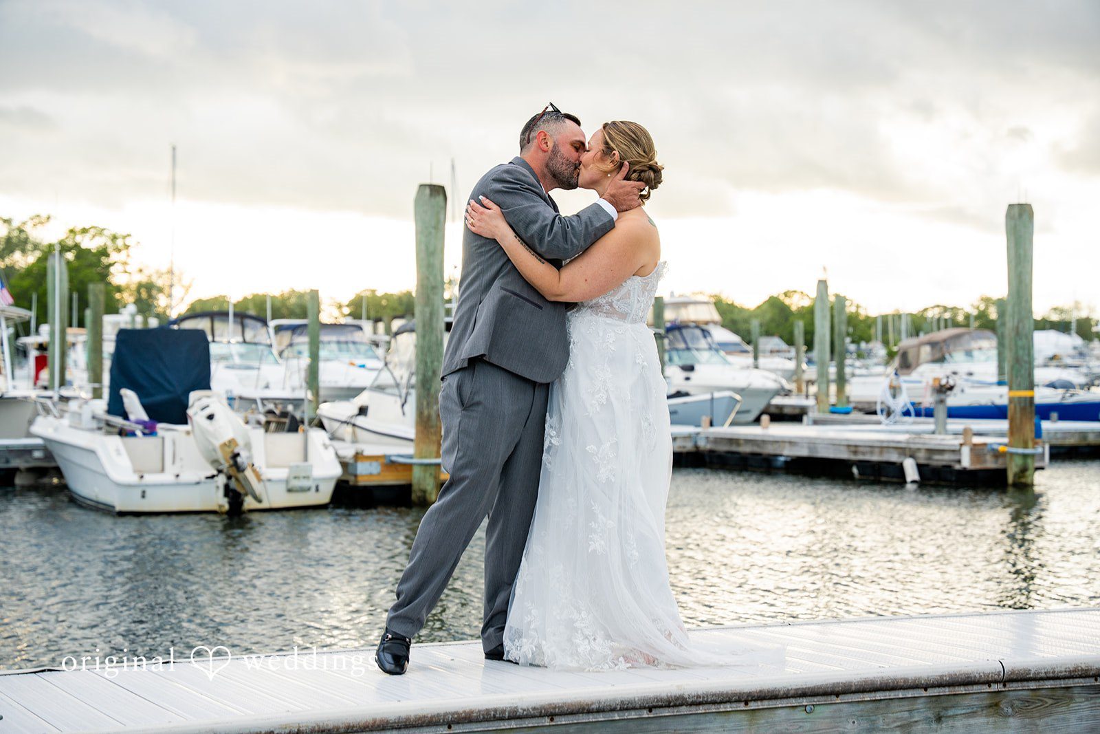 Alex + Courtney A bride and groom embracing and sharing a kiss by a marina.