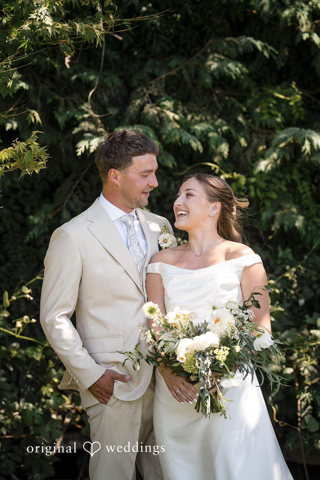 Hanna + Austin A groom and bride smiling together while holding a bouquet.