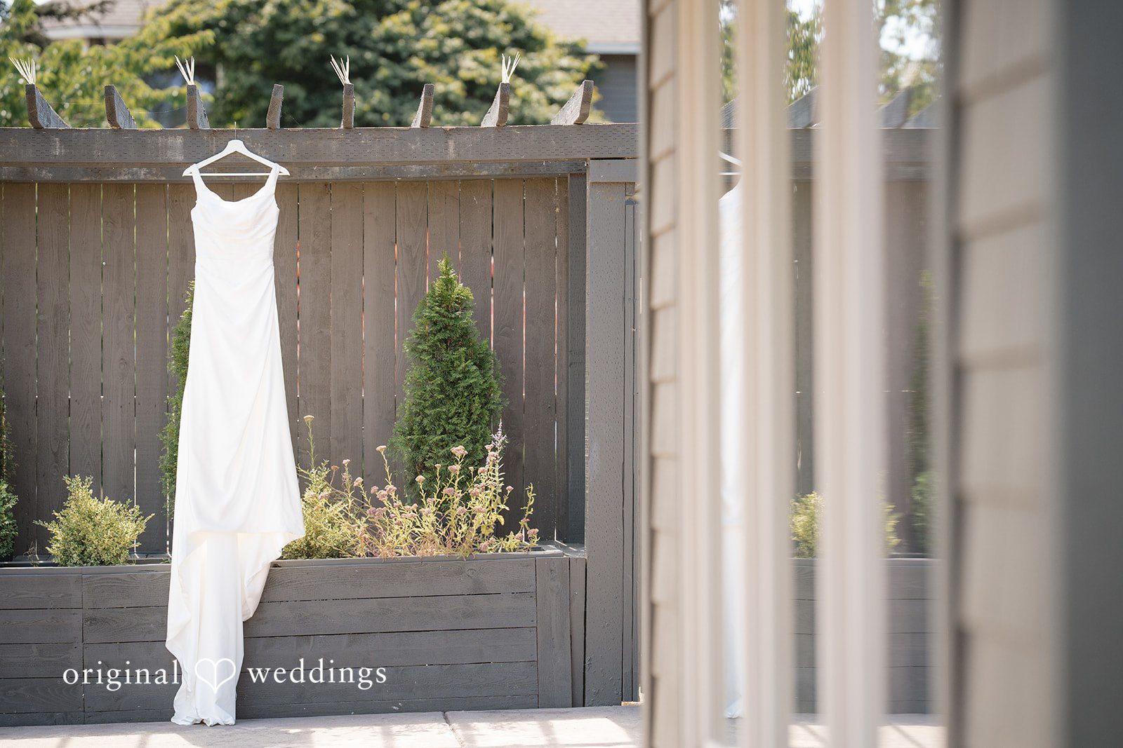 Hanna + Austin A long white wedding dress hanging in a doorway.