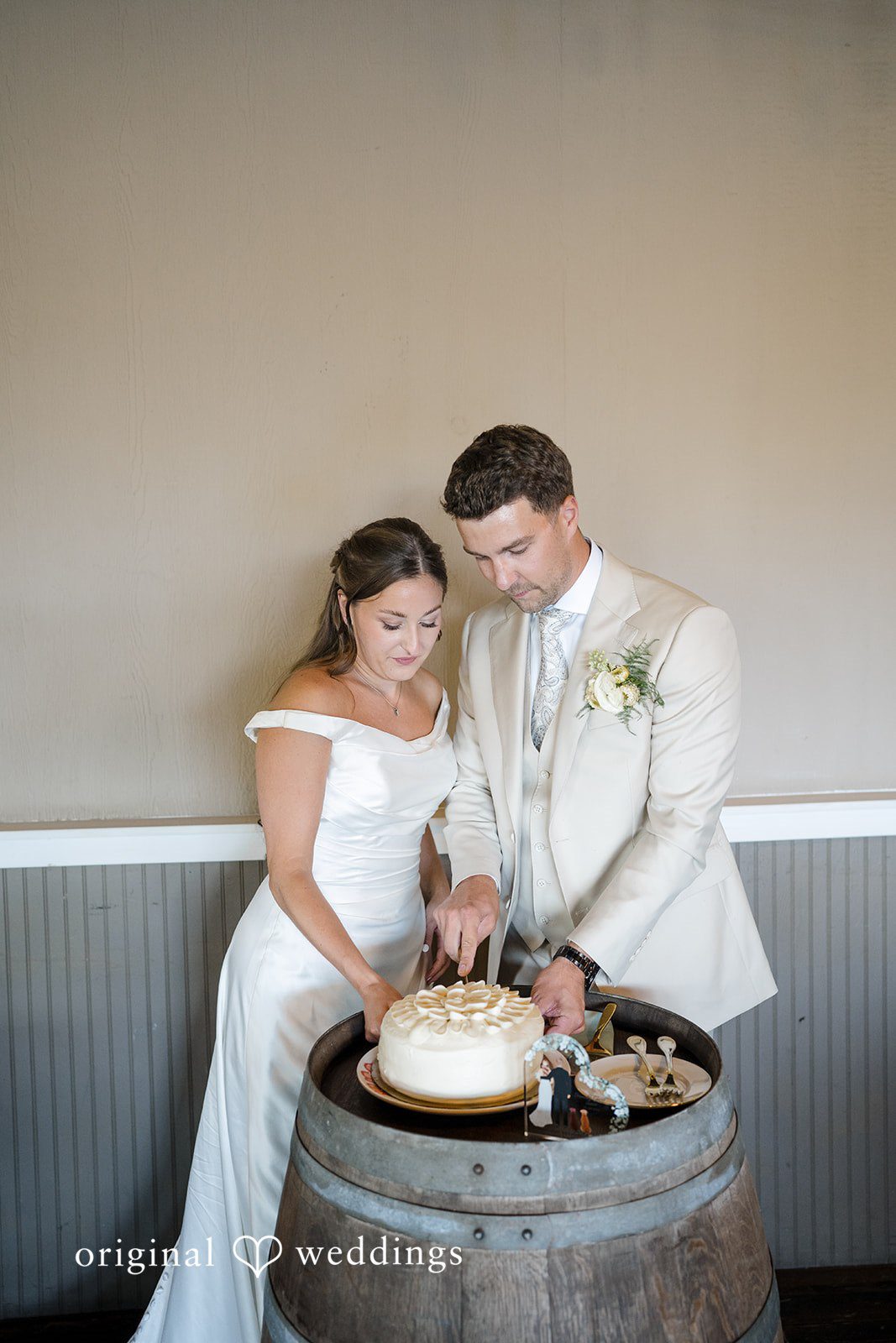 Hanna + Austin A couple cutting their wedding cake placed on top of a wooden barrel.