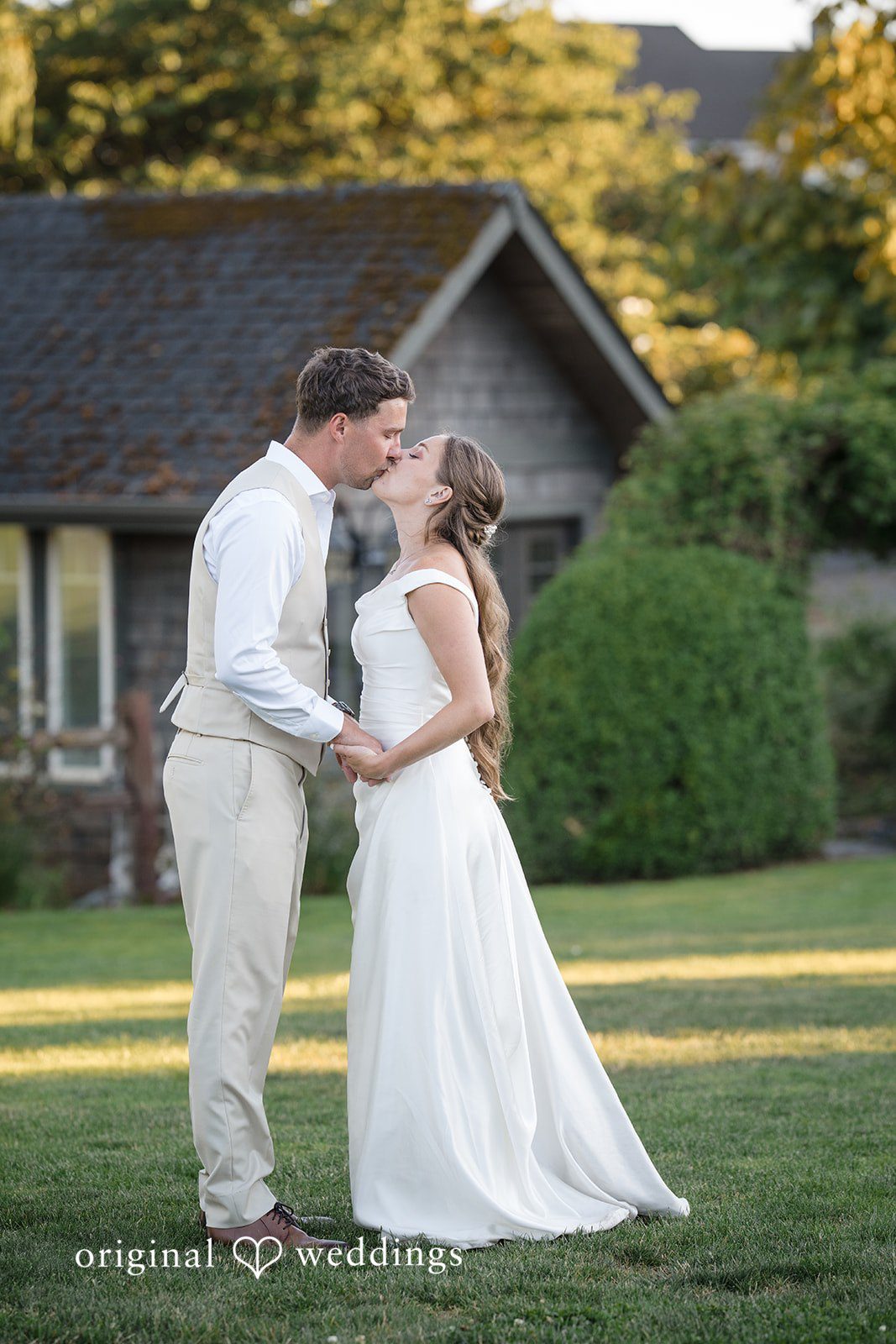 Hanna + Austin A bride and groom kissing on a grassy lawn with a house behind them.