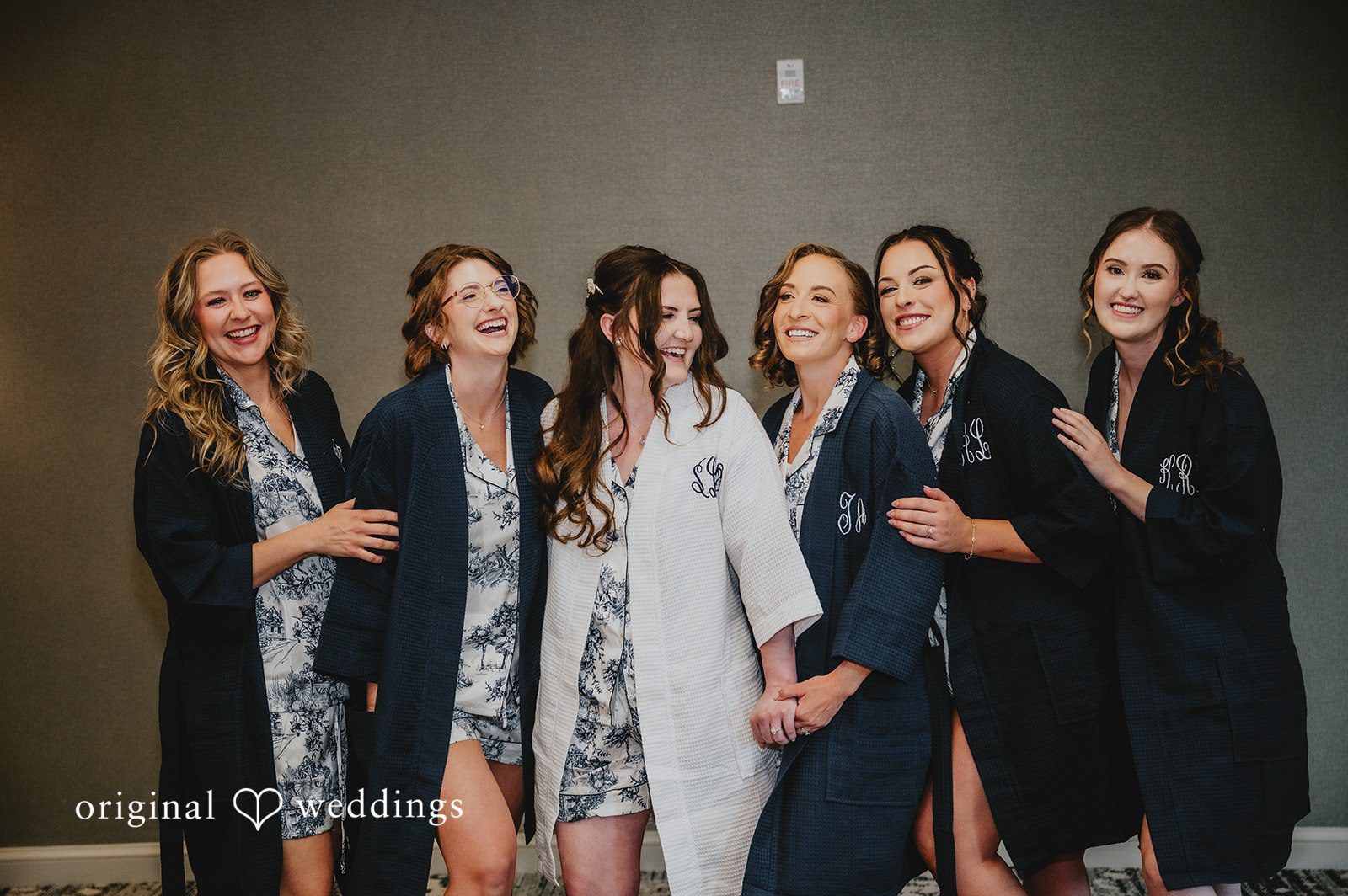 Group of bridesmaids in matching navy and white robes standing together in a room.
