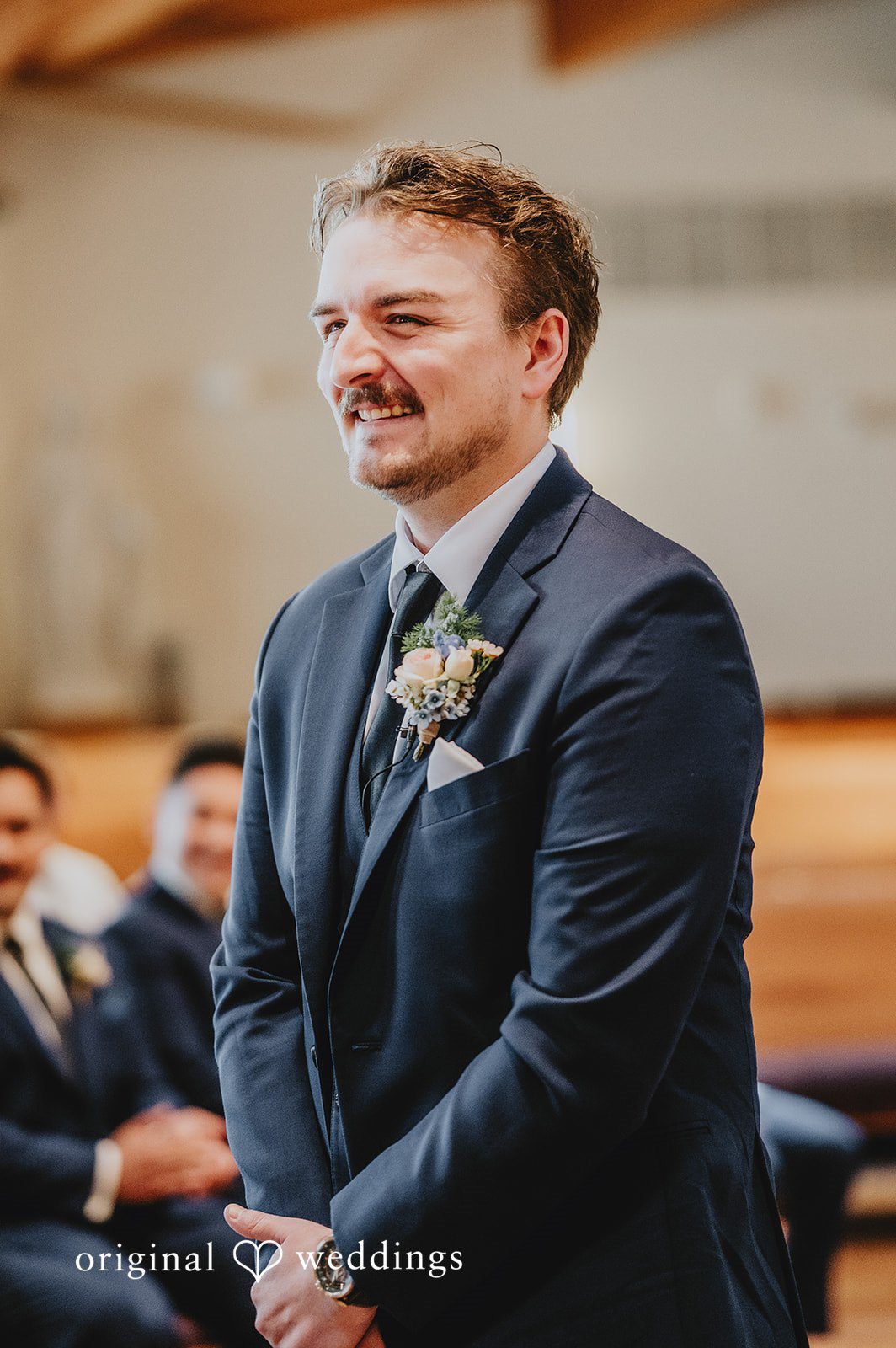 Close-up portrait of a smiling groom in a dark suit with a floral boutonniere.